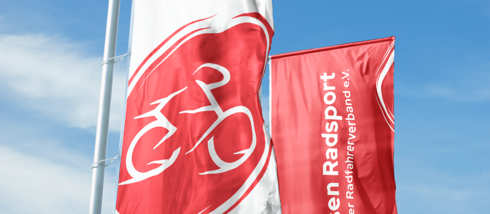 Zwei Fahnen mit Hessen Radsport Logo vor blauem Himmel